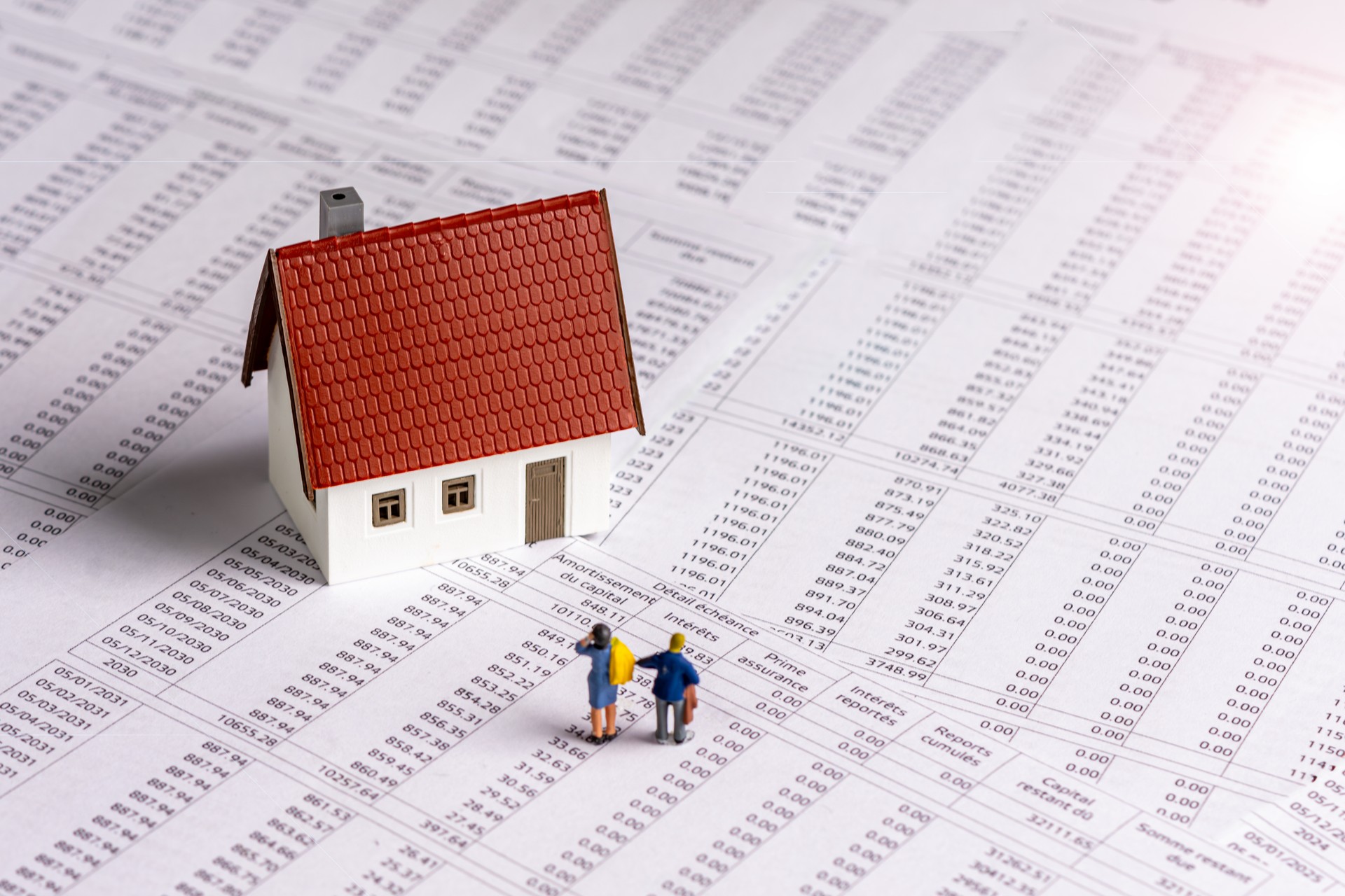 Figurines of a man and a woman and a model house on a French real estate loan schedule document